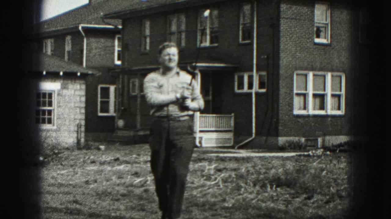 Man holding a golf club in a grassy yard in front of a brick house.