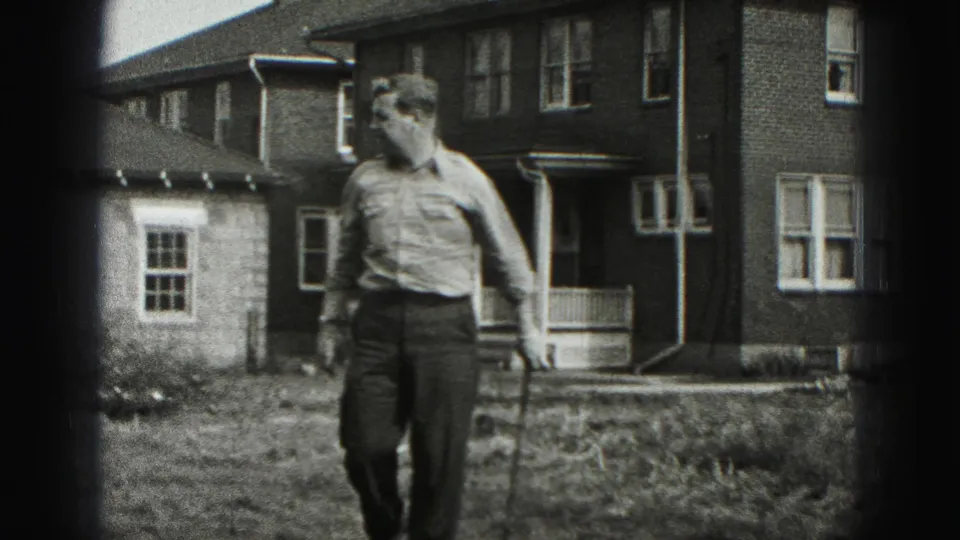 The man leans into his golf stance in a New Cumberland residential yard, with the brick house and porch behind him.