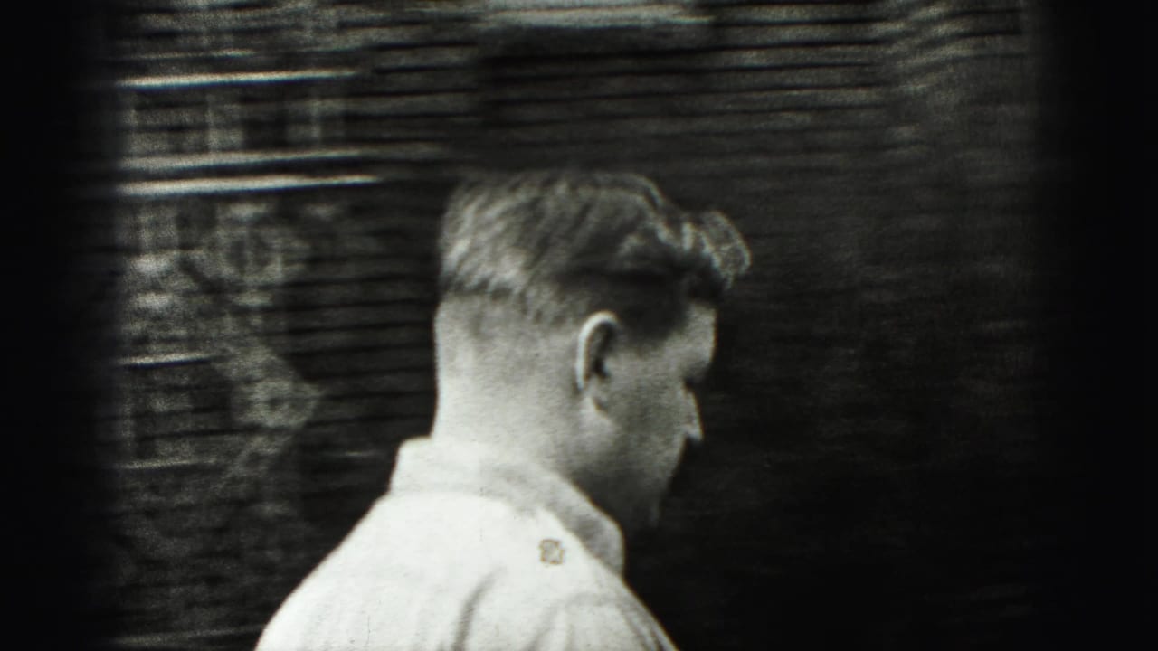 Young man in a light collared shirt walking past a brick wall.