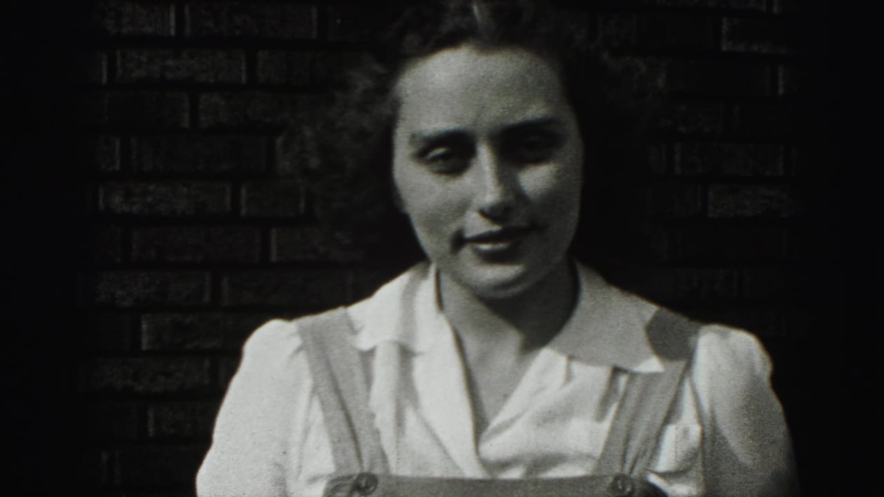Young woman smiles slightly while standing before a brick wall in high-contrast black-and-white footage.