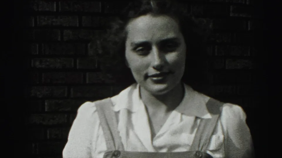 In the 1946 New Cumberland home movie, the woman holds a slight smile before the dark brick wall, with strong shadow across one side of her face.