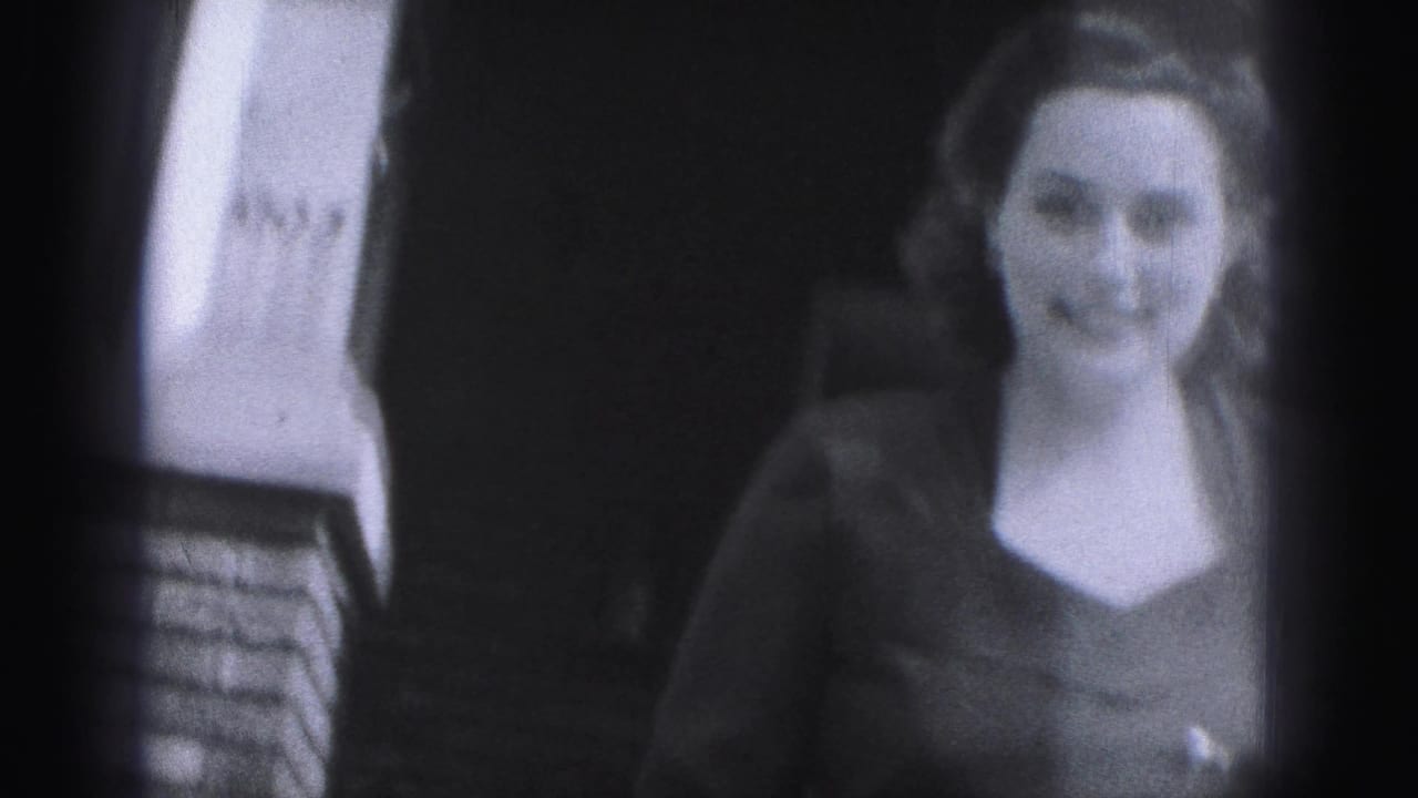 Smiling woman in a dark dress standing near brickwork and a building entrance.