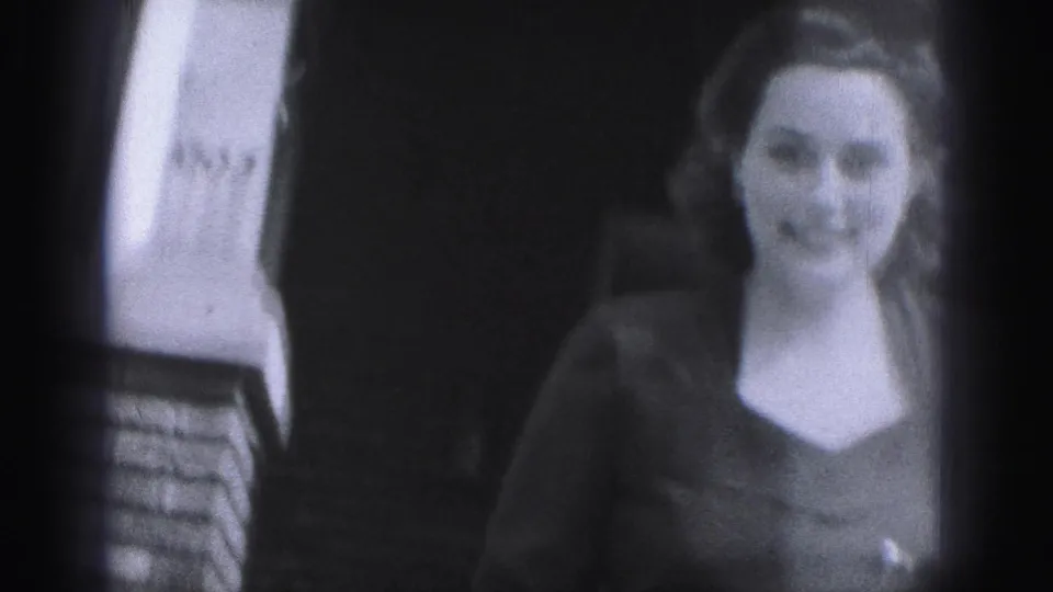 Young woman smiles toward the camera near a brick building in New Cumberland, Pennsylvania, in supported 1946 8mm home-movie footage.