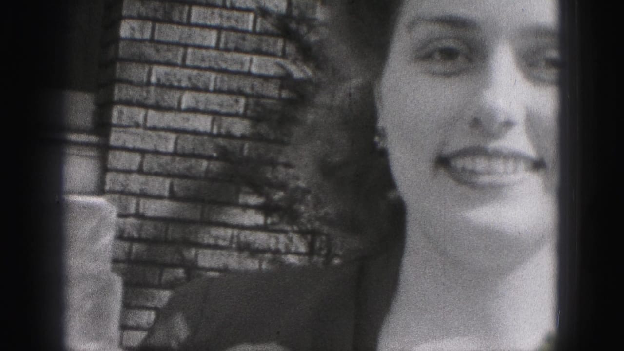 A smiling young woman in a dark dress faces the camera in this 1946 New Cumberland frame, with brickwork and foliage behind her.