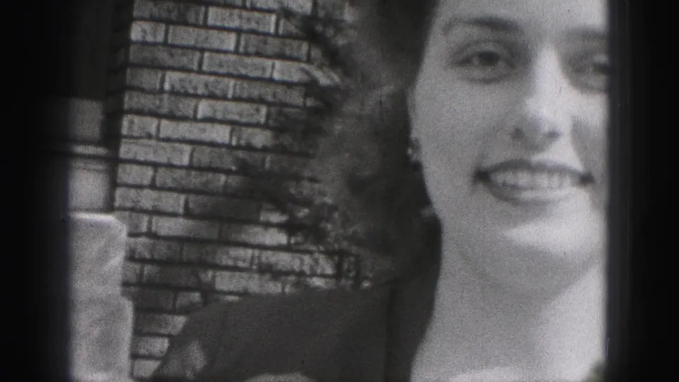 A smiling young woman in a dark dress faces the camera in this 1946 New Cumberland frame, with brickwork and foliage behind her.