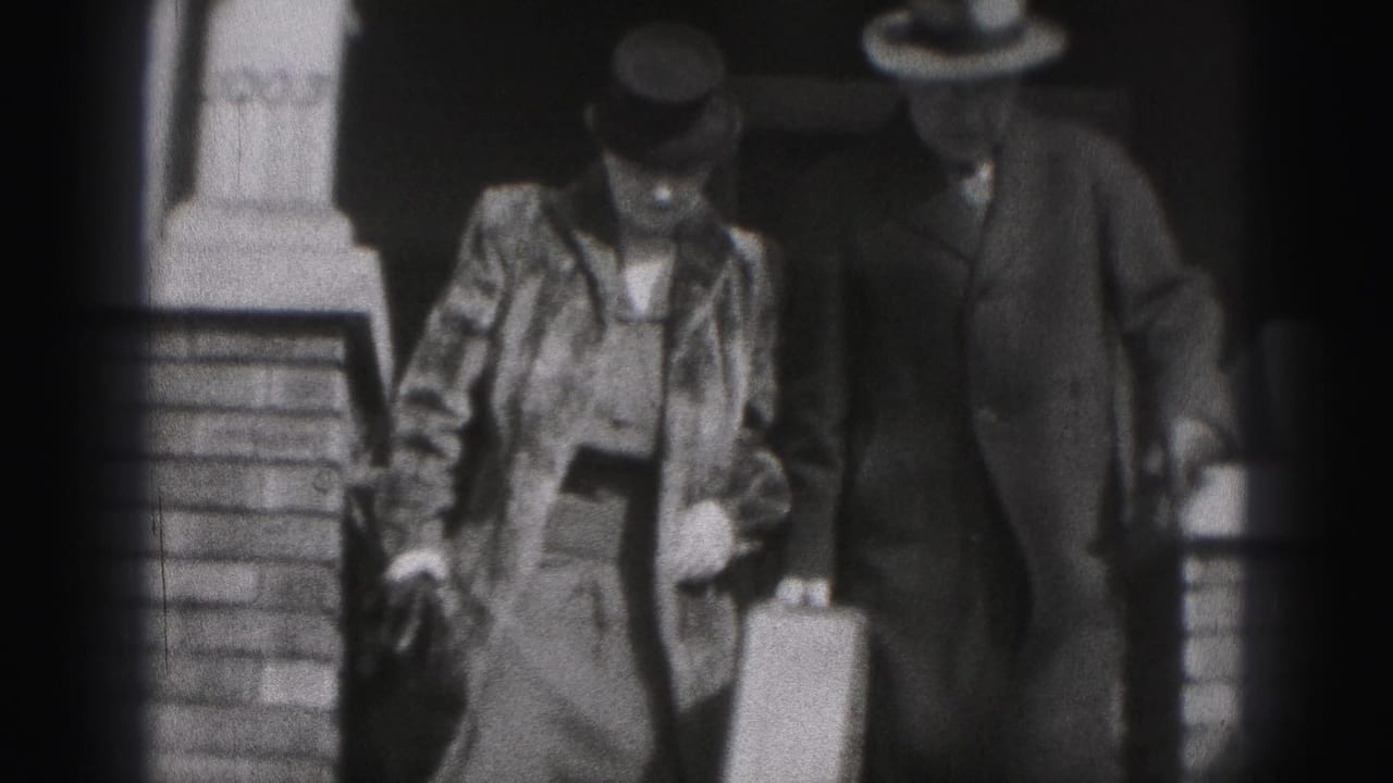 Adult couple in hats walks down exterior steps, with the man carrying a suitcase.
