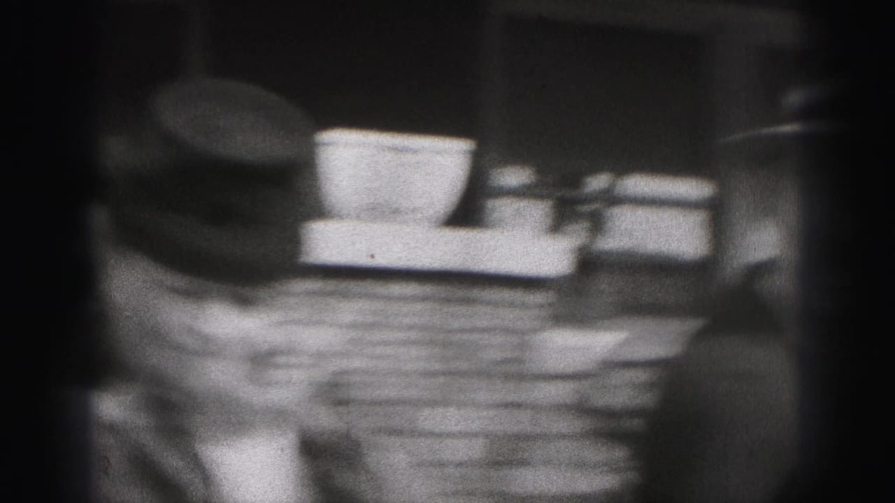 A soft 8mm close view catches the woman's hat and coat beside exterior steps or porch elements in the 1946 home movie.