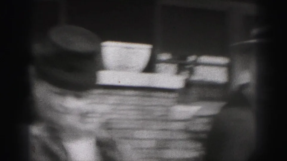 A soft 8mm close view catches the woman's hat and coat beside exterior steps or porch elements in the 1946 home movie.
