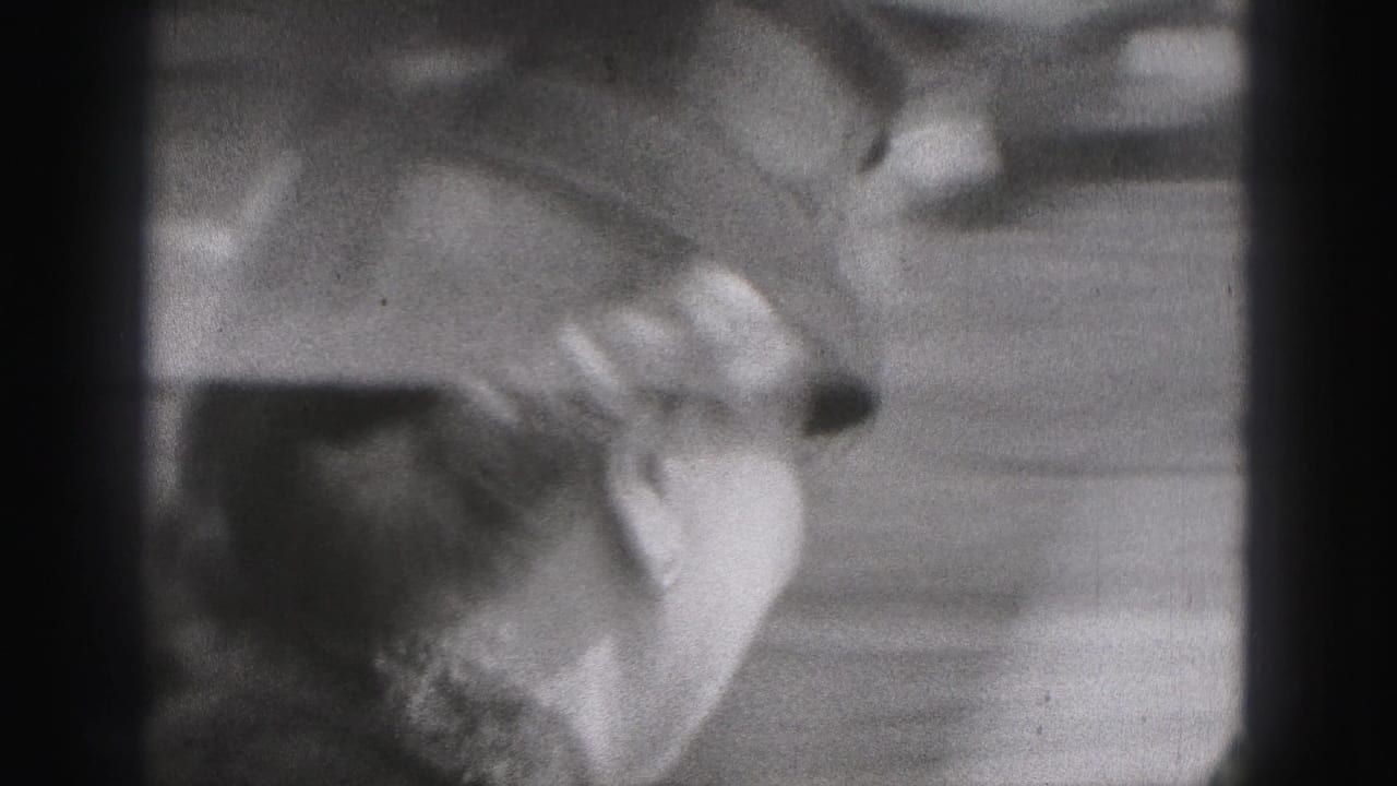 The camera frames the couple closely, with hats and faces visible in soft black-and-white 8mm texture.