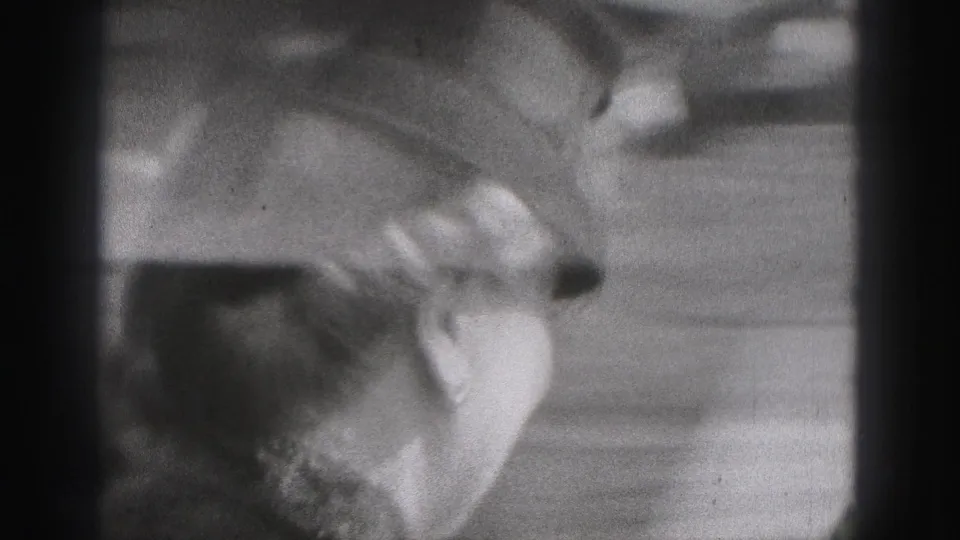 The camera frames the couple closely, with hats and faces visible in soft black-and-white 8mm texture.