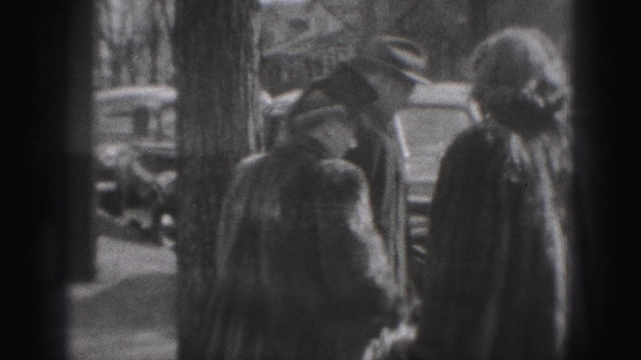 Adults in 1940s attire appear near curbside cars on a New Cumberland street, with leafless trees and houses behind them.