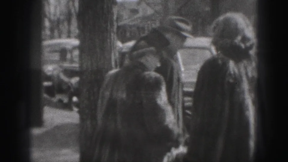 Adults in 1940s attire appear near curbside cars on a New Cumberland street, with leafless trees and houses behind them.