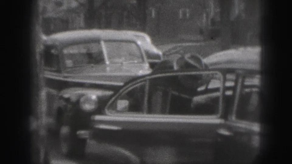 A woman in dark period clothing stands at an open automobile door on a 1946 New Cumberland residential street.