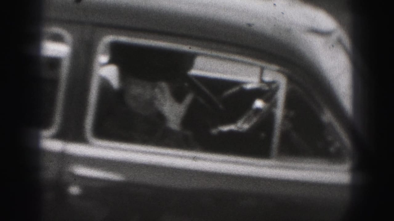 Passenger visible through the side window of a rounded car, with a hand raised inside.