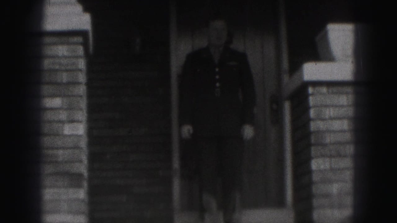 1946 New Cumberland frame showing a man in a dark military-style uniform at the entrance of a brick house.