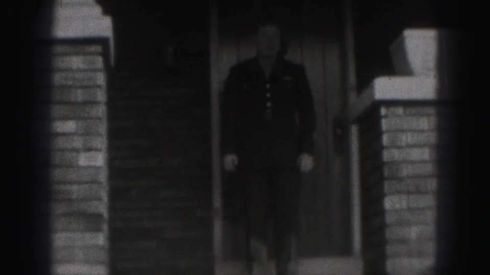 1946 New Cumberland frame showing a man in a dark military-style uniform at the entrance of a brick house.