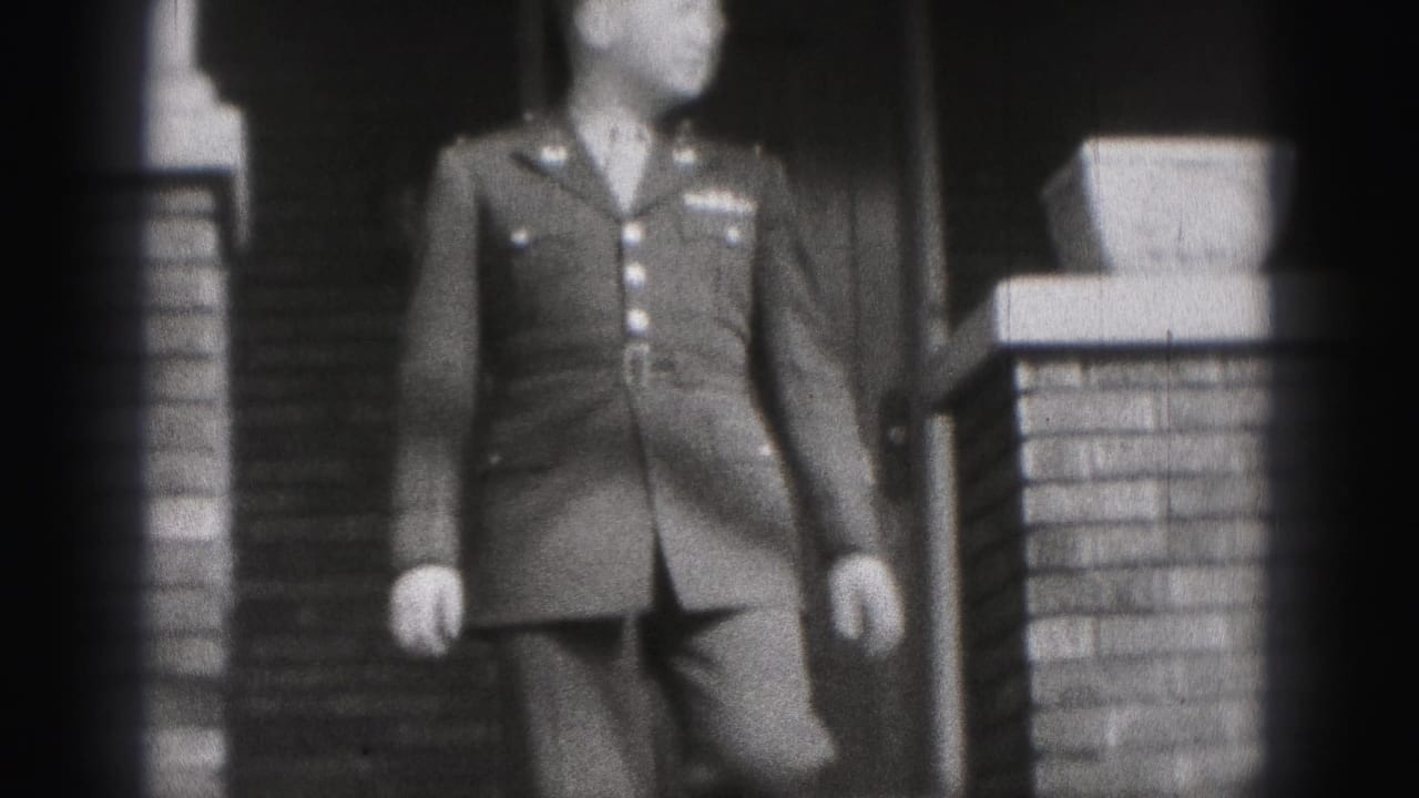The man in formal military uniform continues down the house steps, partly soft from the 8mm home-movie focus.