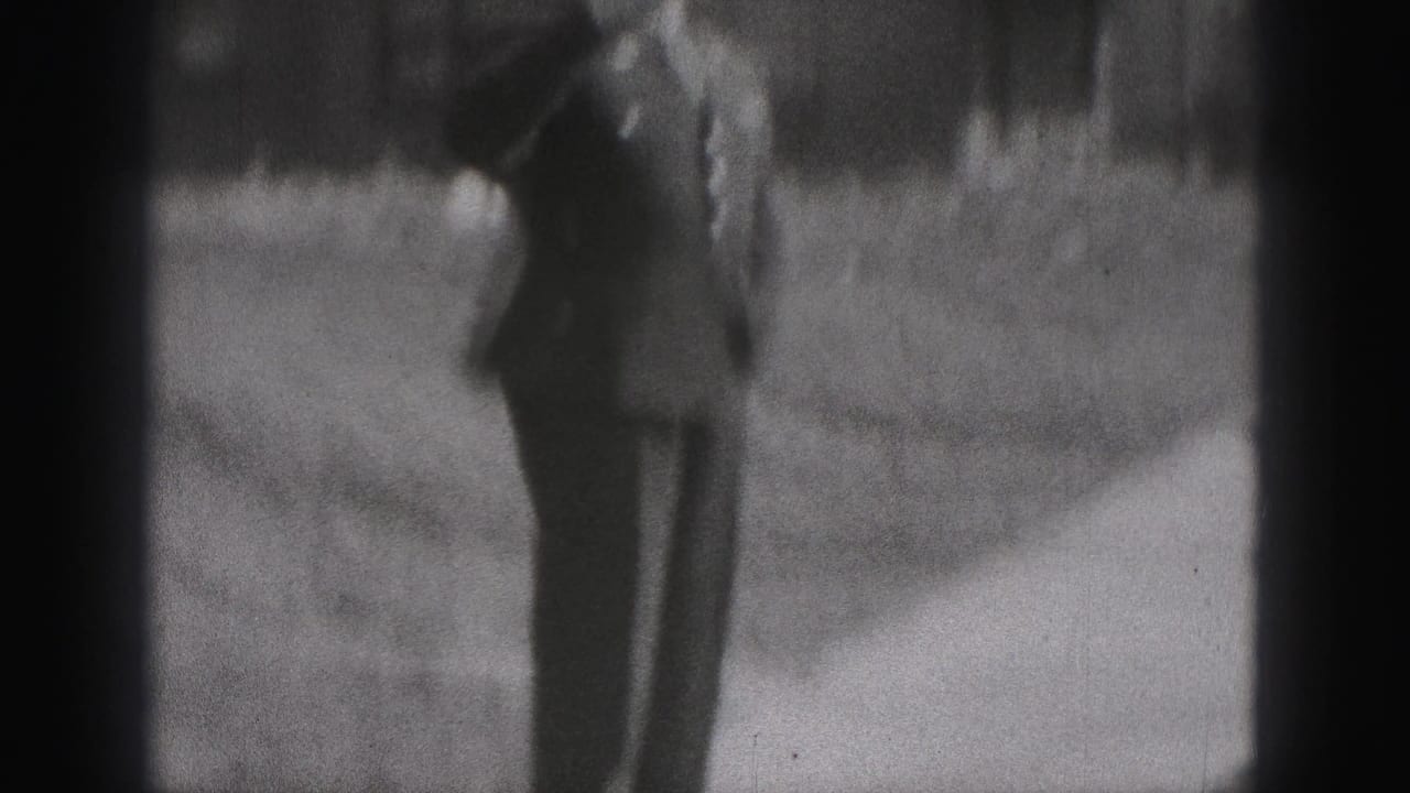 In 1946 New Cumberland home-movie footage, a man in dark formal clothing walks beside a grass verge and residential building.