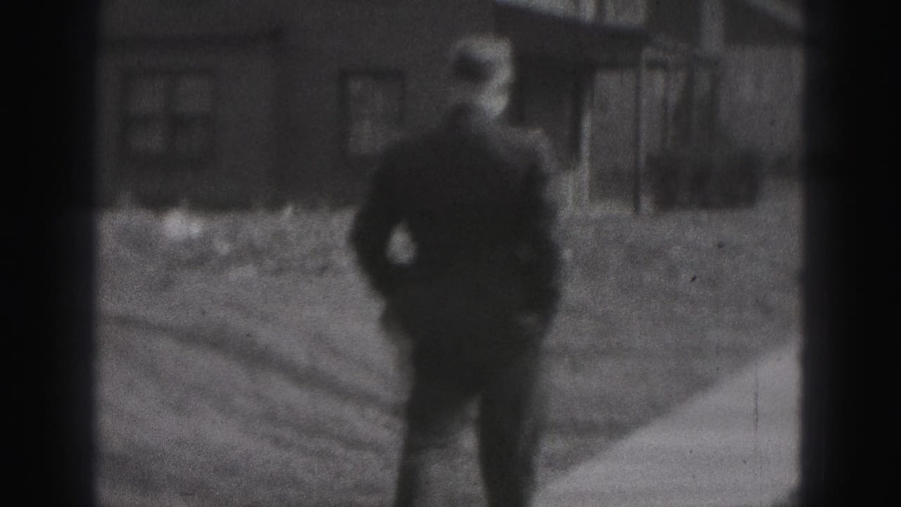 Man in dark clothing seen from behind on a sidewalk beside a residential building.