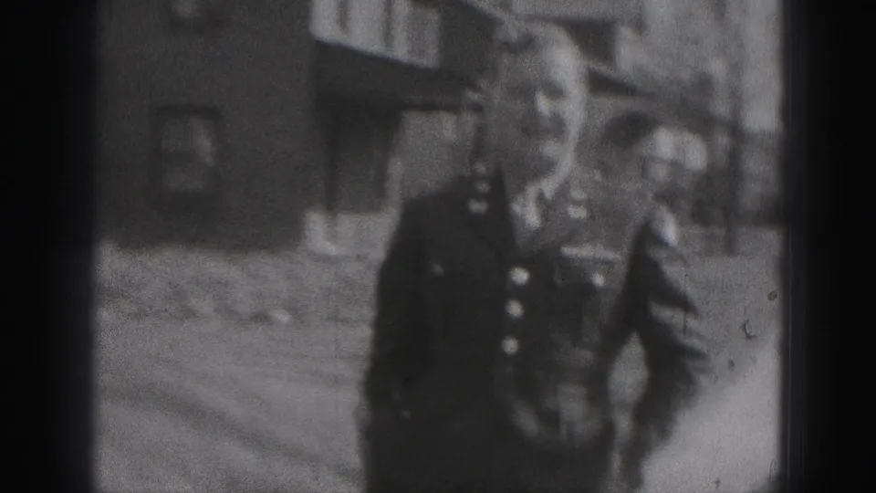 The man faces the camera more closely, with buttons and uniform-like details visible against a residential New Cumberland backdrop.