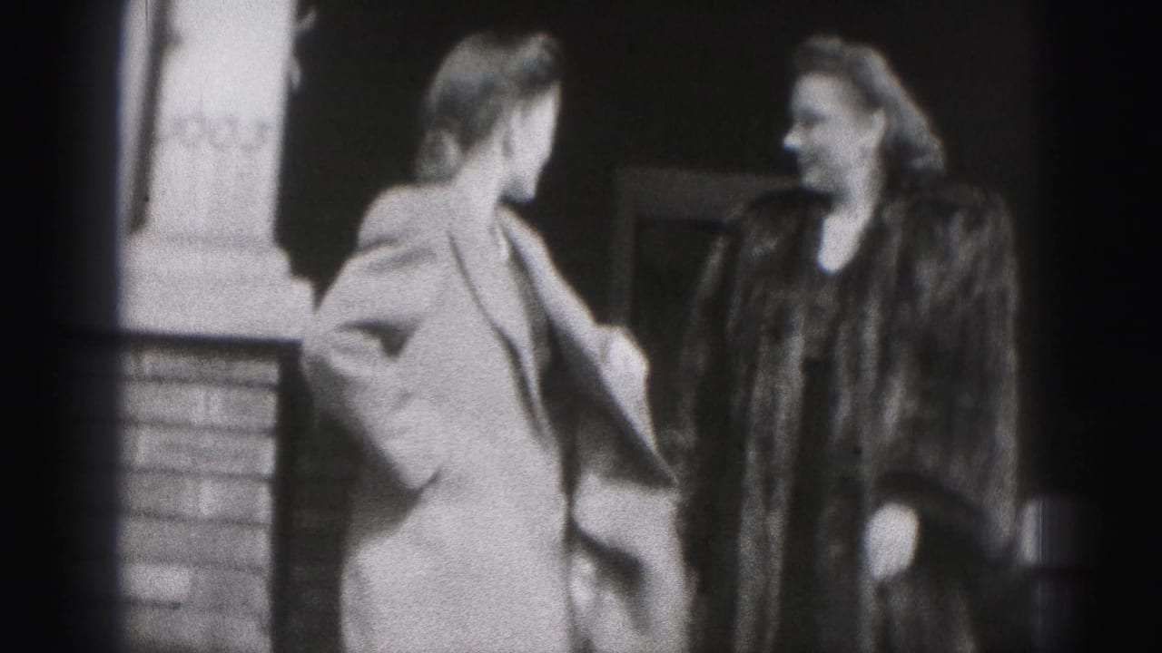 Two women in coats smile near a brick building entrance.