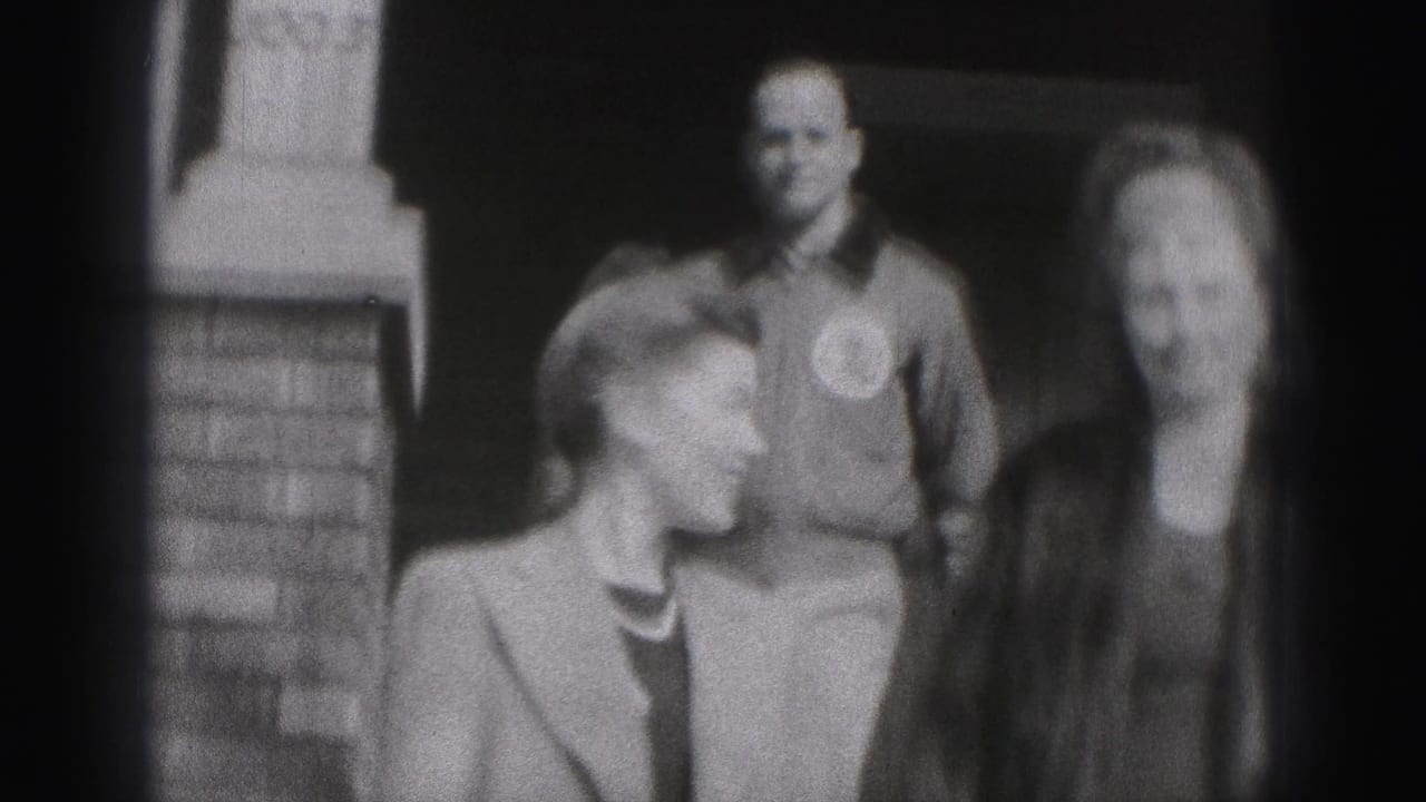In the New Cumberland home movie, two women stand in front of a smiling man near a brick doorway, with faces partly softened by motion blur.