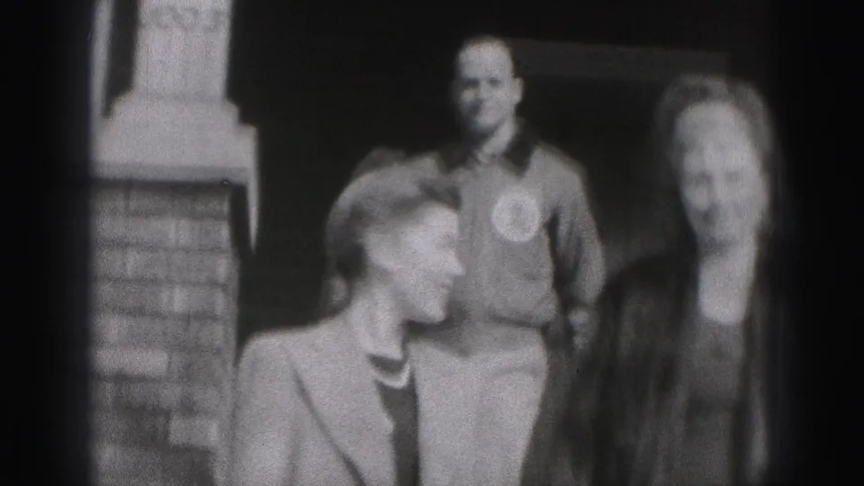 In the New Cumberland home movie, two women stand in front of a smiling man near a brick doorway, with faces partly softened by motion blur.