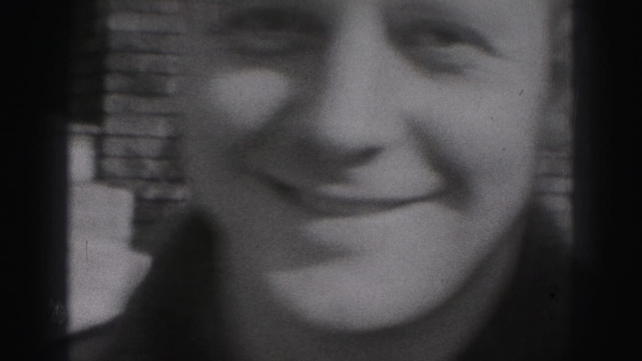 A tightly framed 1946 home-movie close-up shows a smiling young face with brickwork visible in the background.