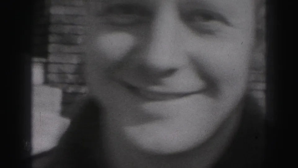 A tightly framed 1946 home-movie close-up shows a smiling young face with brickwork visible in the background.