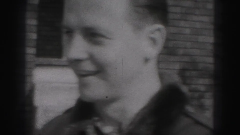 A young man in the 1946 New Cumberland home movie smiles in profile near a brick wall, filmed in soft black-and-white 8mm.
