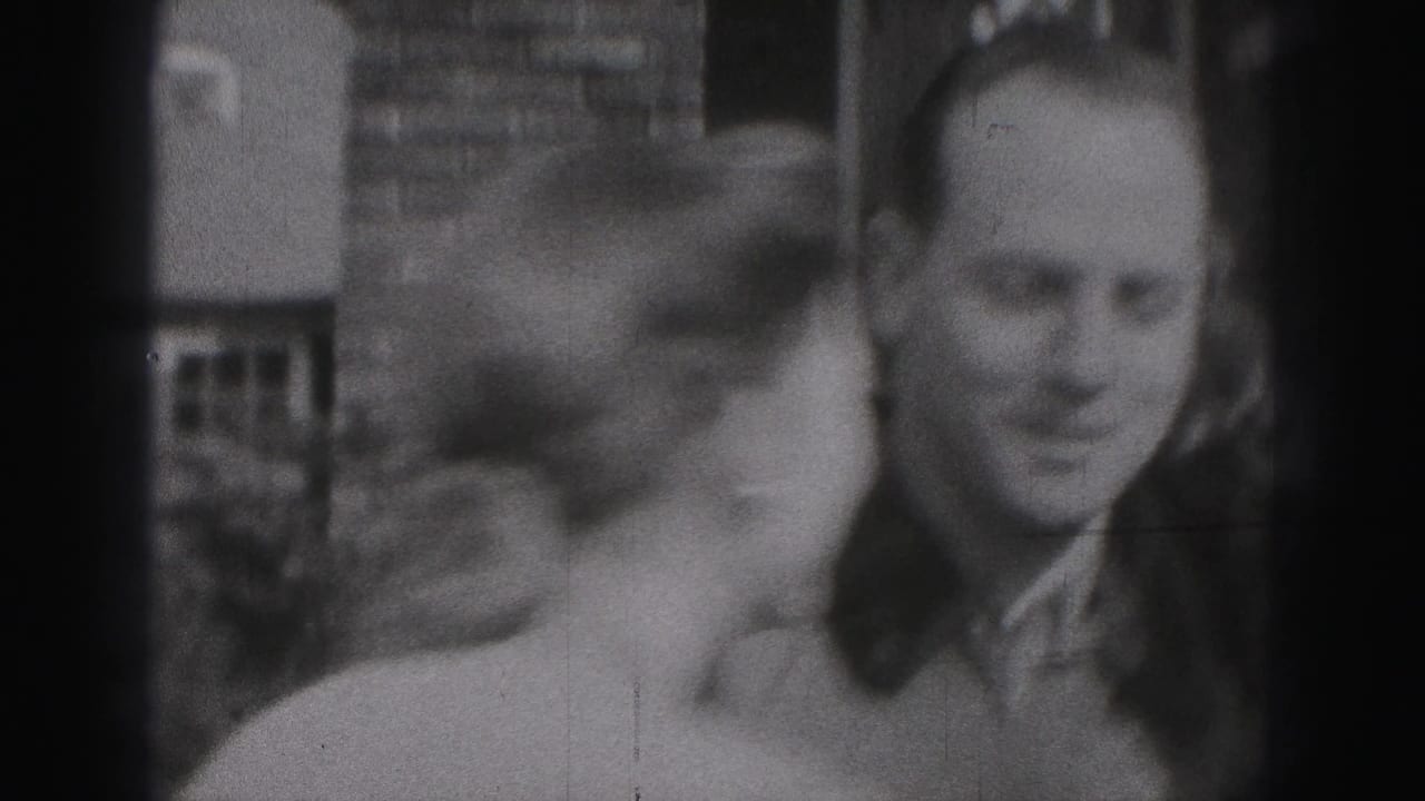 A woman leans toward a smiling man outdoors near a building.