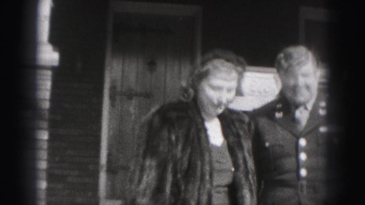 Uniformed man and woman in a dark coat standing together outside a brick home.