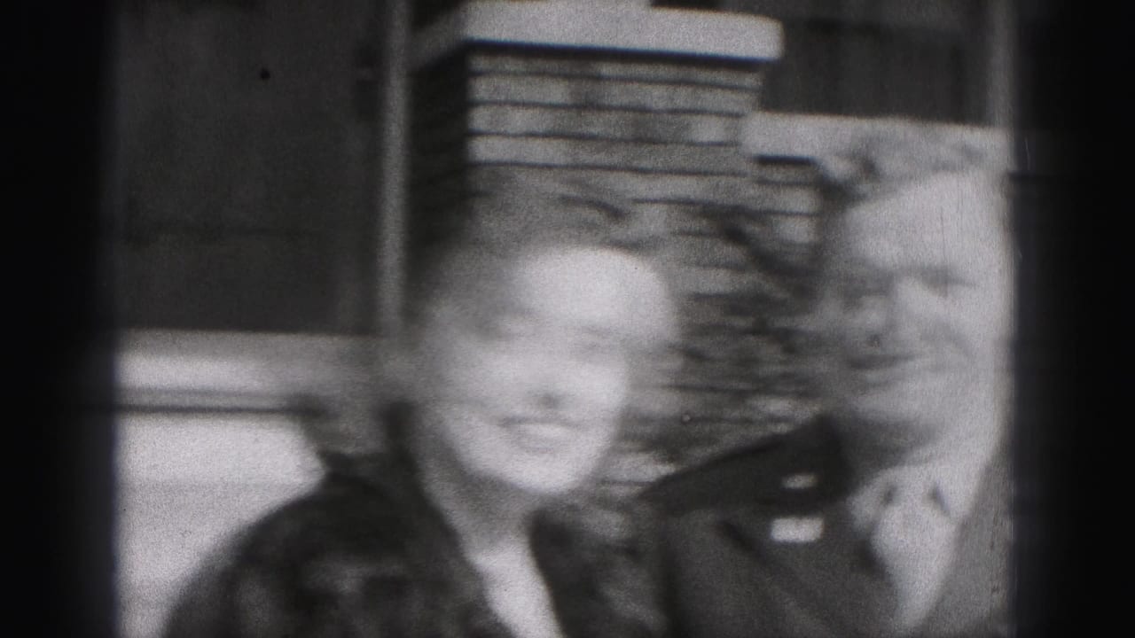 The woman smiles toward the camera while standing beside the uniformed man outside the New Cumberland home, with brickwork behind them.