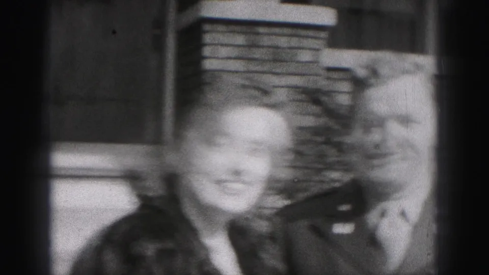 The woman smiles toward the camera while standing beside the uniformed man outside the New Cumberland home, with brickwork behind them.