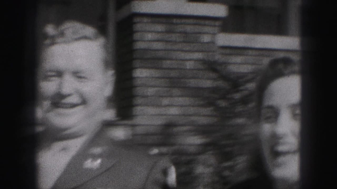 A smiling uniformed man and woman stand close together in front of a brick house wall in this 1946 New Cumberland home-movie frame.