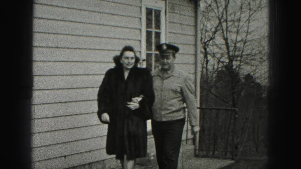 In New Cumberland, Pennsylvania, a woman in a dark coat and a man in a uniform-style cap walk together outside a house in 1946 home-movie footage.
