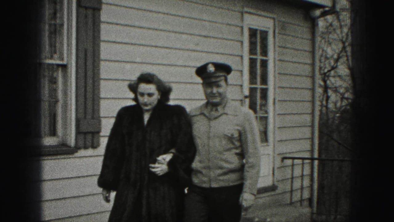 Smiling couple walks close together past a shuttered window and house siding.