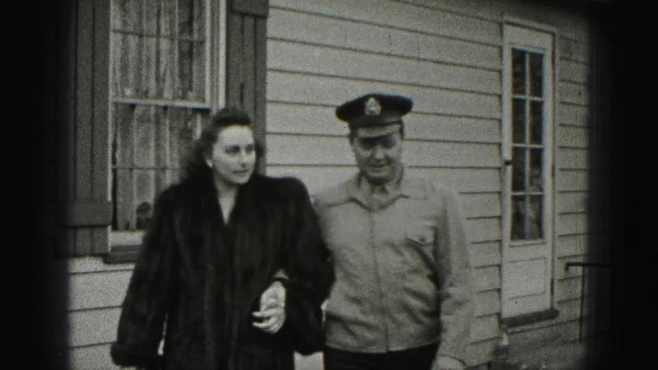 A closer 1946 home-movie frame shows the couple walking past shuttered windows, with the woman holding the man's arm.