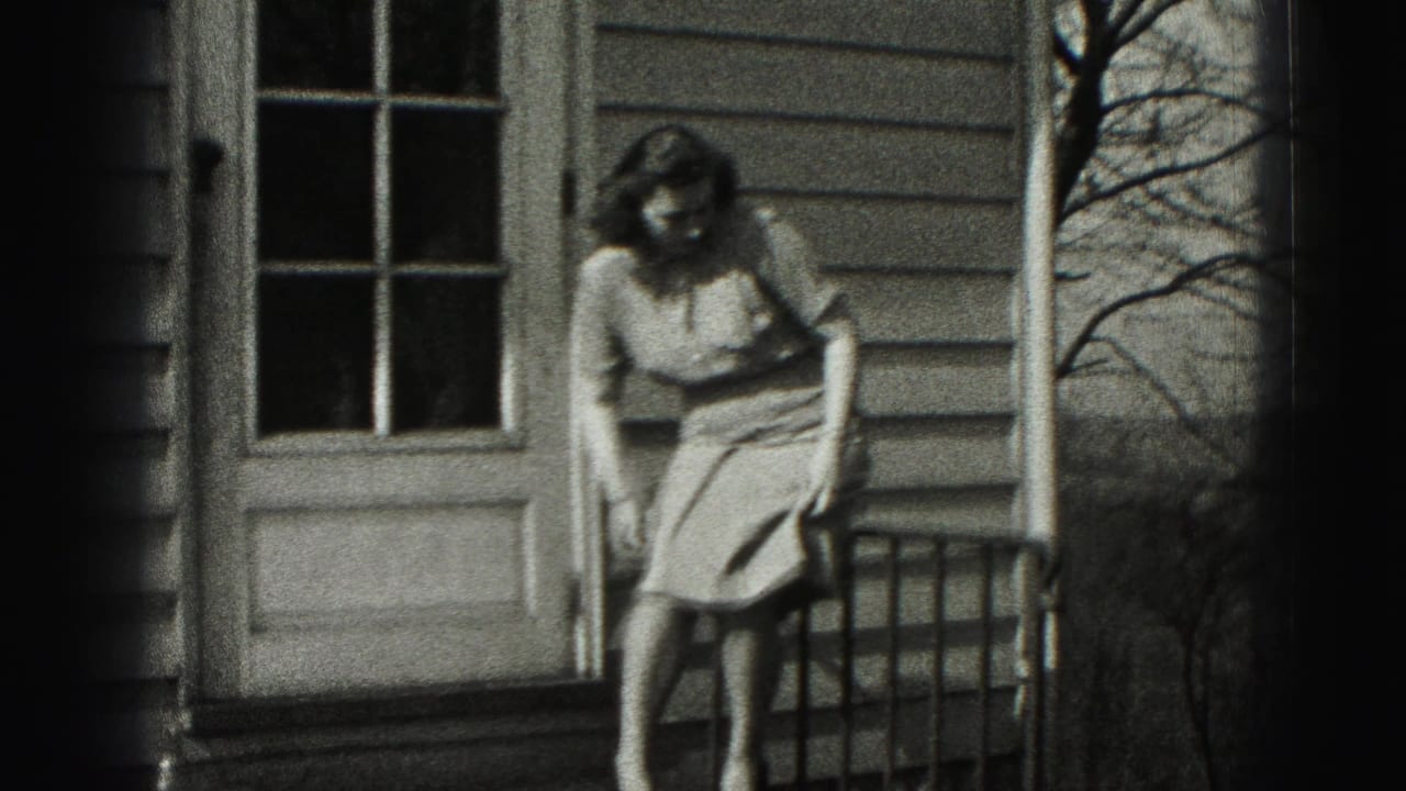 Woman sits or lowers herself near a porch railing beside a house door.