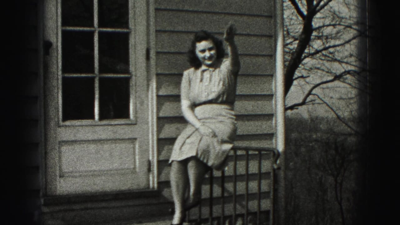 The seated woman smiles and waves toward the camera from a residential porch in 1946 New Cumberland home-movie footage.