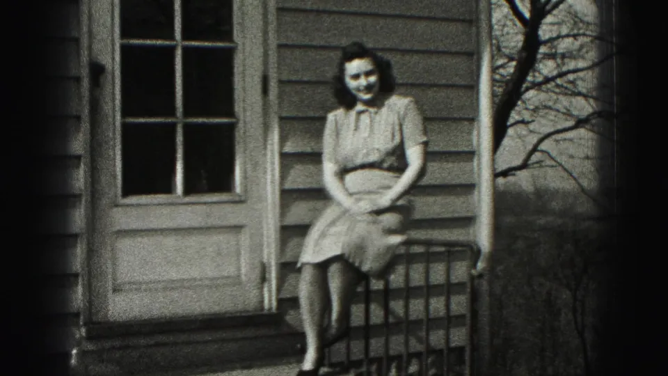 Woman in a 1940s-style dress sits on a porch railing outside a house in New Cumberland, Pennsylvania.