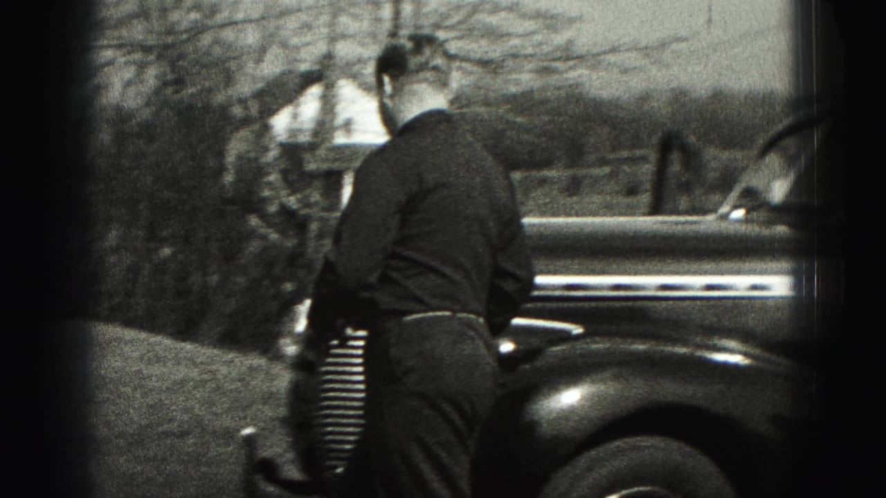 Man seen from behind approaches the front of a rounded sedan near a house and trees in New Cumberland.