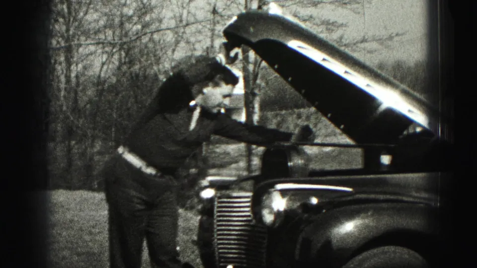 In 1946 New Cumberland, Pennsylvania footage, a suited man bends over the open hood of a 1940s automobile beside bare trees.