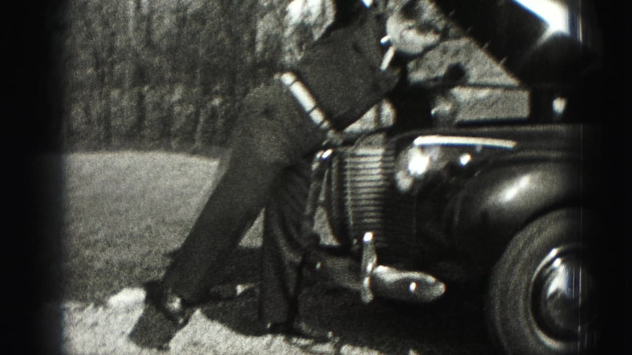 The man stands near the raised hood and front grille of a vintage automobile in the 1946 Pennsylvania home-movie scene.