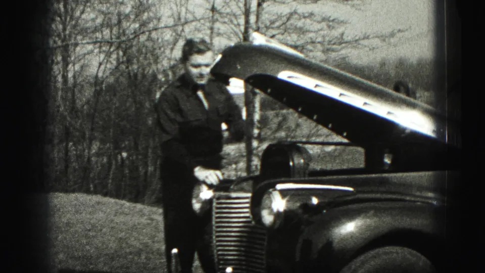 In 1946 New Cumberland, Pennsylvania, a man stands near the open hood of a classic car in a suburban yard.
