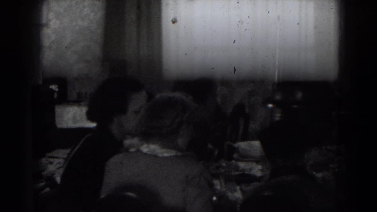 In a 1947 Lincoln, Nebraska home-movie frame, adults sit around a dim dining table near a bright window.
