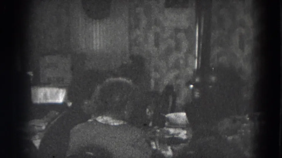 Adults appear at a dining table inside a Lincoln, Nebraska home, with patterned wallpaper and dishes visible.