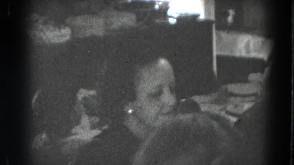 A seated adult is visible near a set dining table in grainy 1947 Lincoln, Nebraska home footage.