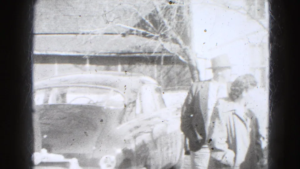 In 1947 Lincoln, Nebraska, adults in period coats gather beside a parked dark automobile outside a residence.