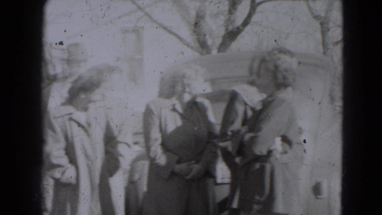 Adults in 1940s coats and hats stand together near a vehicle in the Lincoln, Nebraska home-movie scene.